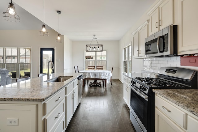 kitchen featuring a sink, decorative backsplash, stainless steel appliances, a center island with sink, and dark wood-type flooring