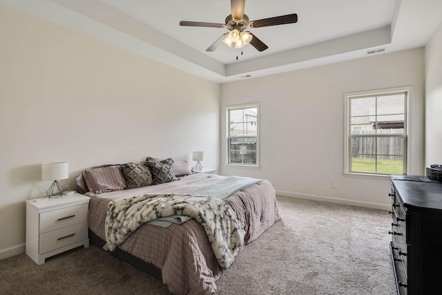 bedroom featuring a ceiling fan, carpet floors, a tray ceiling, baseboards, and visible vents