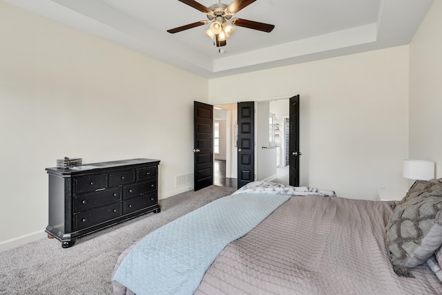 bedroom with a raised ceiling, visible vents, a ceiling fan, baseboards, and carpet flooring