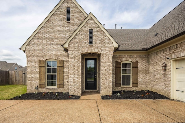 entrance to property with brick siding, fence, a shingled roof, and a garage
