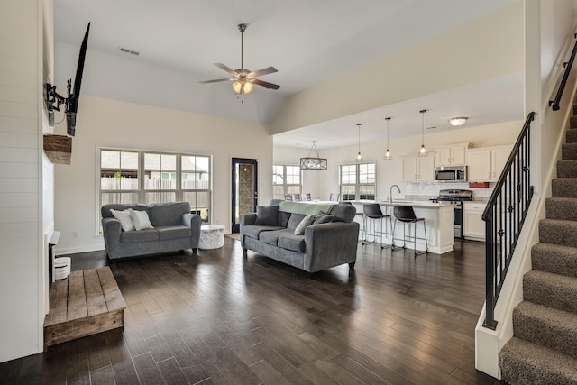 living area featuring stairway, visible vents, dark wood-type flooring, high vaulted ceiling, and ceiling fan