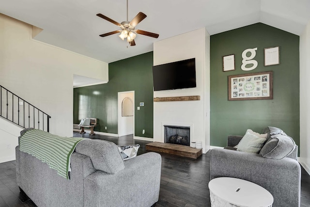 living area featuring stairway, vaulted ceiling, ceiling fan, a fireplace, and dark wood-style floors