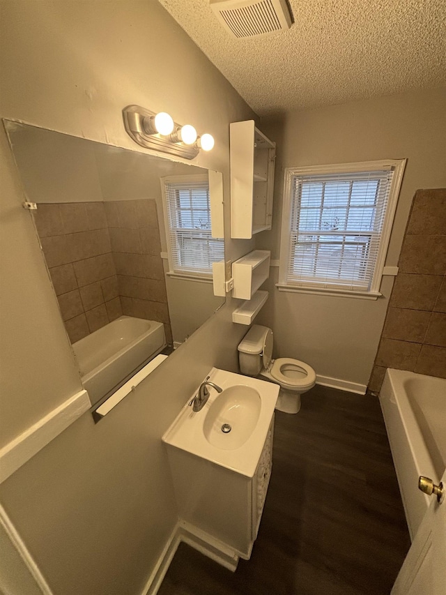 full bathroom with wood finished floors, visible vents, toilet, a healthy amount of sunlight, and a textured ceiling