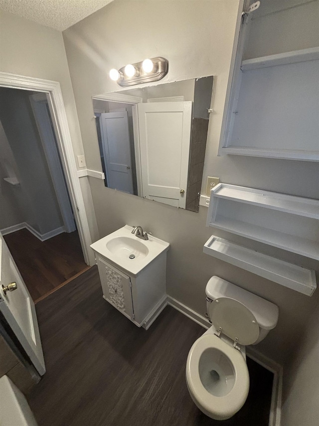 half bathroom with wood finished floors, a textured ceiling, vanity, and toilet
