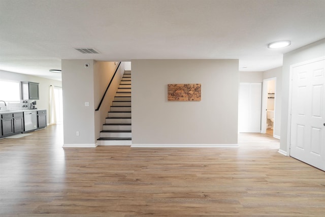 unfurnished living room with stairway, visible vents, a sink, baseboards, and light wood-style flooring