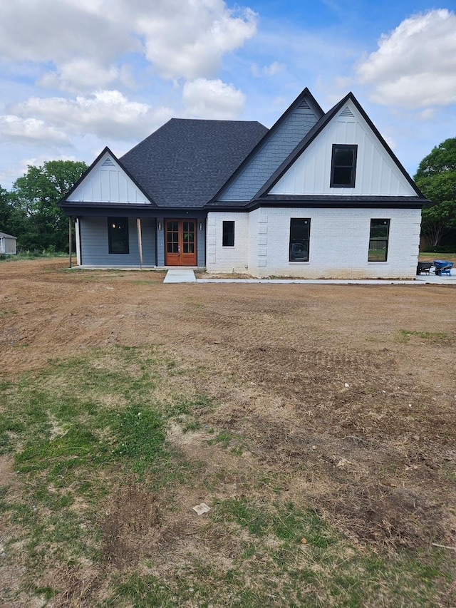 modern farmhouse style home with board and batten siding, french doors, roof with shingles, and brick siding