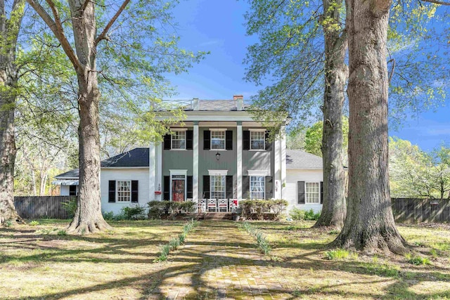 greek revival inspired property with a porch, a chimney, and fence
