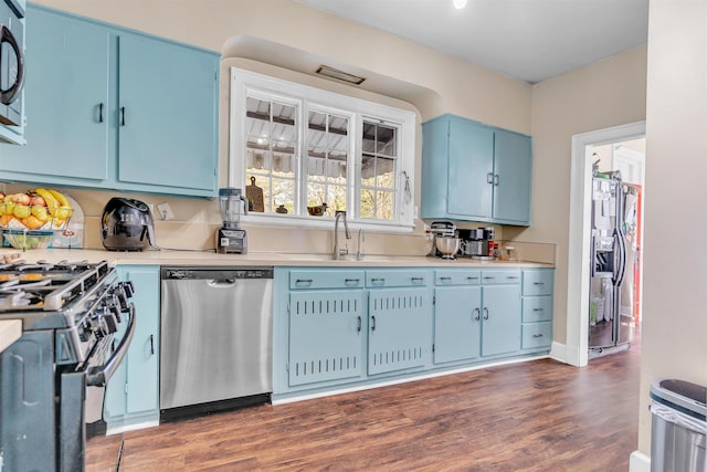 kitchen featuring a sink, stainless steel appliances, light countertops, dark wood finished floors, and blue cabinetry