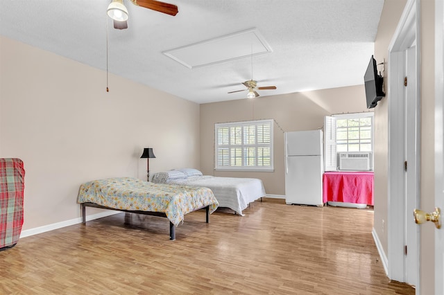 bedroom with attic access, freestanding refrigerator, wood finished floors, and multiple windows