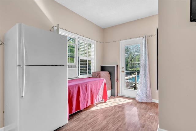 bedroom with wood finished floors, freestanding refrigerator, access to outside, and multiple windows