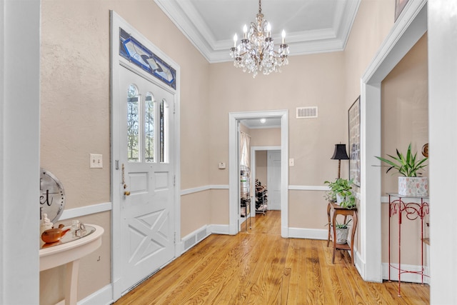 foyer with light wood-style flooring, visible vents, crown molding, and an inviting chandelier