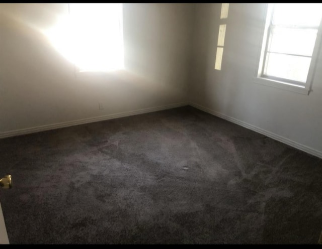 spare room featuring dark carpet and baseboards