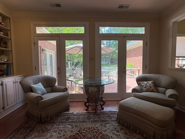 living area with crown molding, wood finished floors, and visible vents