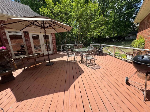 wooden deck with outdoor dining space, french doors, and a grill