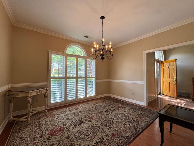 unfurnished dining area featuring crown molding, wood finished floors, a chandelier, baseboards, and visible vents