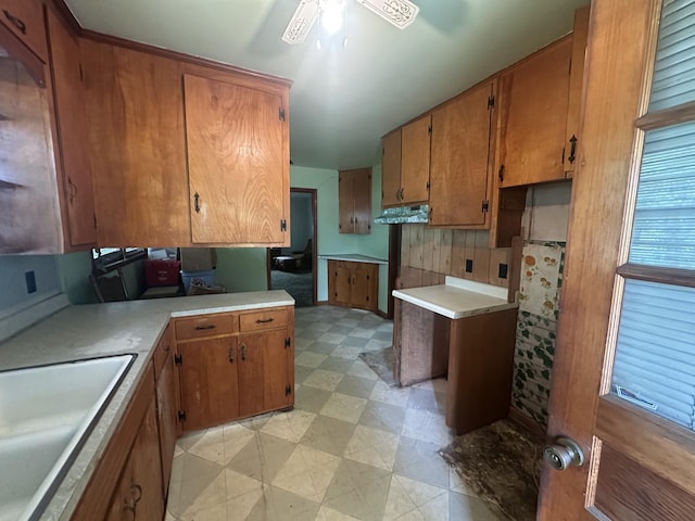 kitchen featuring brown cabinets, under cabinet range hood, a sink, and light floors