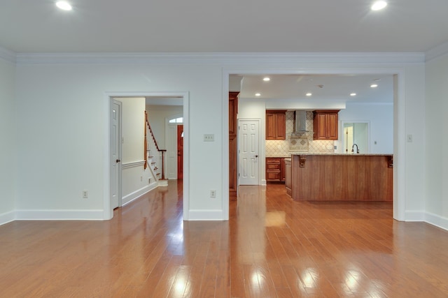 kitchen featuring wall chimney exhaust hood, wood finished floors, backsplash, and brown cabinets
