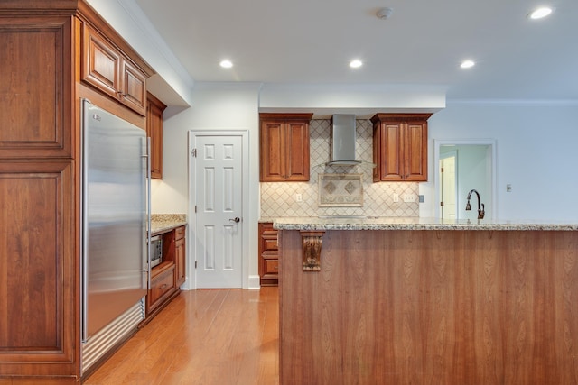 kitchen featuring backsplash, ornamental molding, light wood-type flooring, wall chimney exhaust hood, and appliances with stainless steel finishes