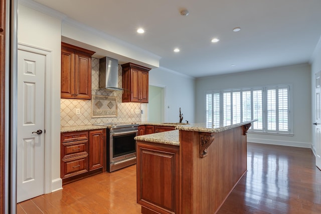 kitchen featuring a sink, backsplash, stainless steel range with electric stovetop, wall chimney range hood, and a breakfast bar area