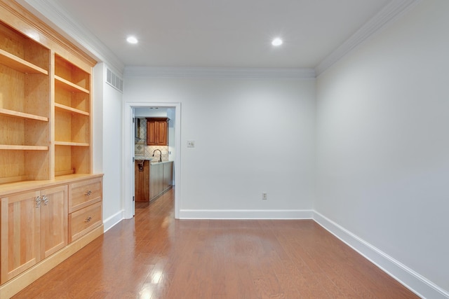 unfurnished room featuring wood finished floors, visible vents, a sink, crown molding, and baseboards