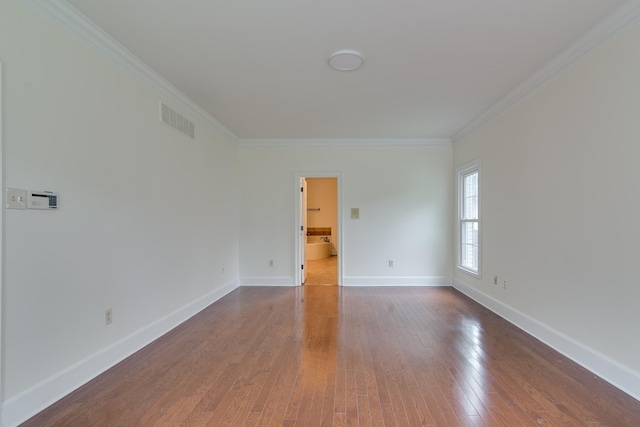 empty room featuring baseboards, crown molding, wood finished floors, and visible vents