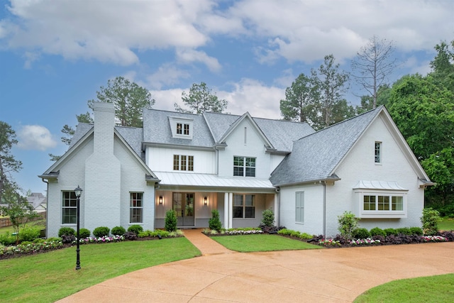 modern farmhouse style home with brick siding, a front lawn, a chimney, and a standing seam roof
