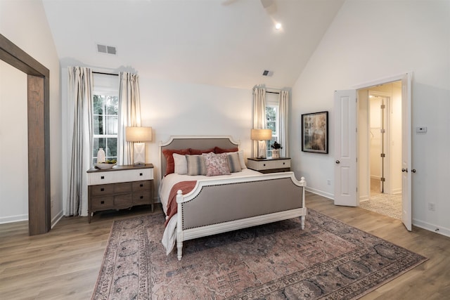 bedroom featuring high vaulted ceiling, baseboards, light wood-style floors, and visible vents