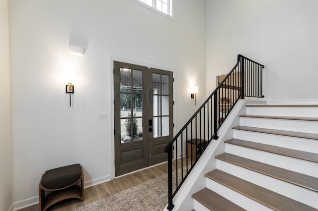 foyer with a towering ceiling, wood finished floors, french doors, baseboards, and stairs
