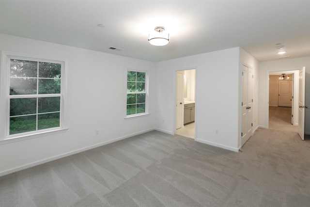 unfurnished bedroom featuring visible vents, baseboards, connected bathroom, and light colored carpet