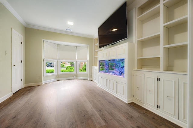 unfurnished living room featuring baseboards, wood finished floors, visible vents, and crown molding