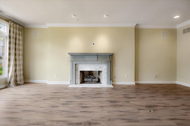 unfurnished living room featuring wood finished floors, a wealth of natural light, a high end fireplace, and crown molding