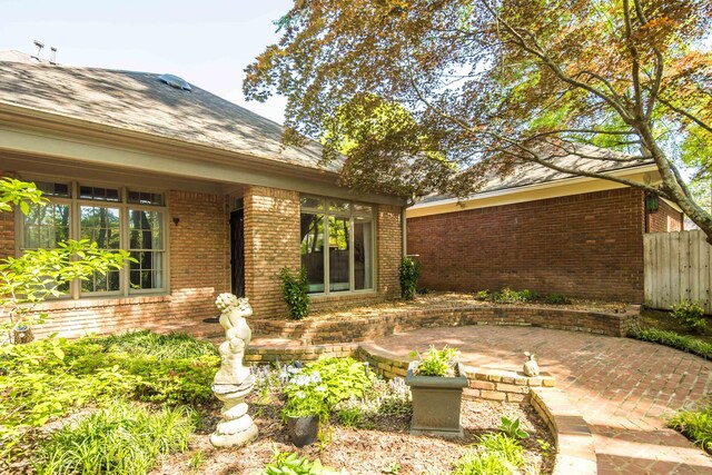 exterior space featuring brick siding, a shingled roof, a patio, and fence