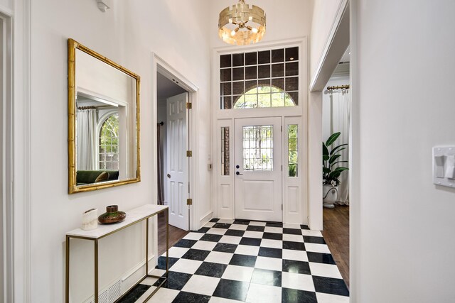 foyer entrance with dark floors, a towering ceiling, baseboards, and a notable chandelier