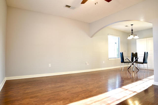 spare room featuring dark wood-style floors, arched walkways, baseboards, visible vents, and ceiling fan with notable chandelier