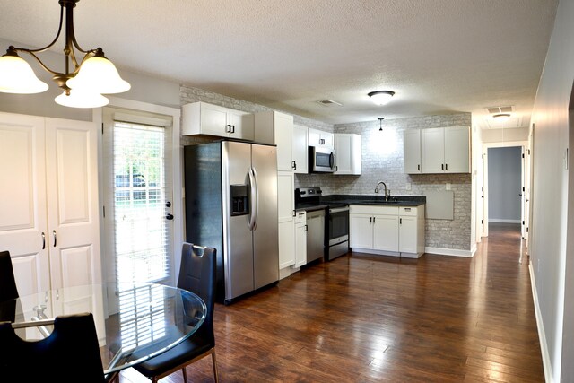 kitchen featuring stainless steel appliances, dark countertops, a sink, a chandelier, and white cabinetry