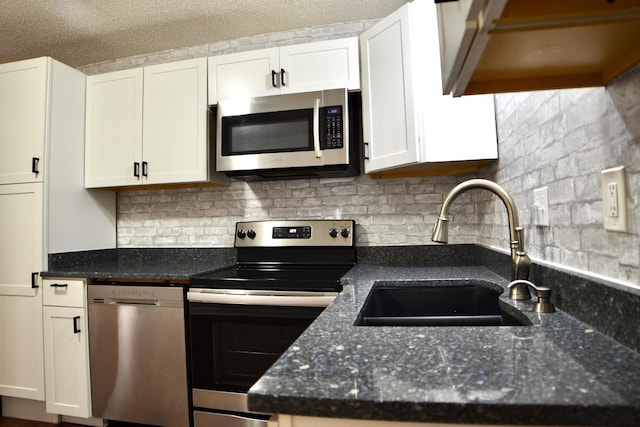 kitchen with a sink, dark stone countertops, tasteful backsplash, white cabinetry, and appliances with stainless steel finishes