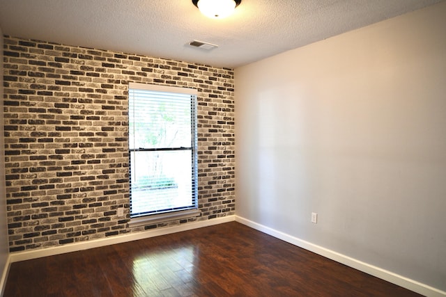 unfurnished room featuring visible vents, brick wall, baseboards, and dark wood-style flooring