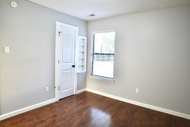 unfurnished room with baseboards, dark wood-style flooring, and visible vents