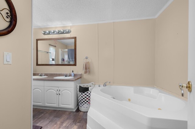 full bathroom with a whirlpool tub, wood finished floors, ornamental molding, a sink, and a textured ceiling