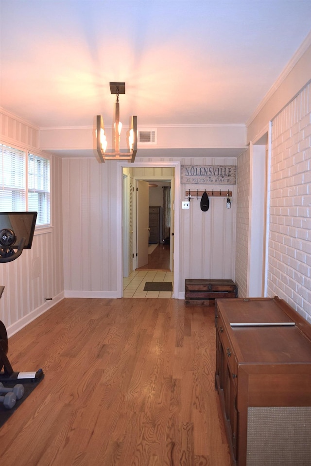 unfurnished dining area featuring light wood-type flooring, visible vents, a notable chandelier, and ornamental molding