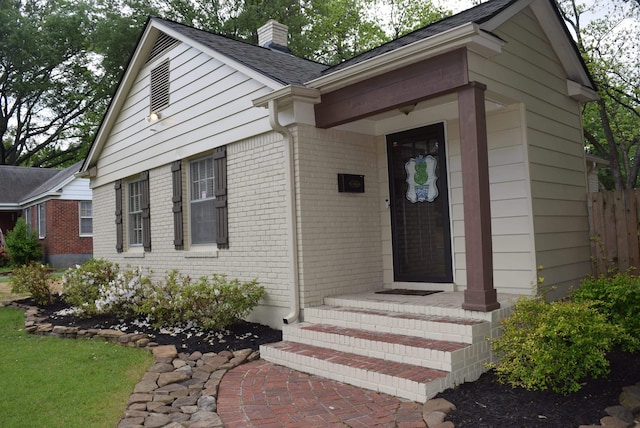 property entrance with fence, a chimney, brick siding, and roof with shingles