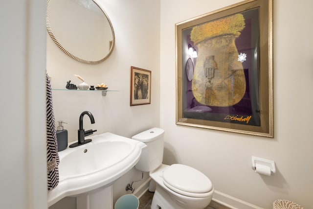 half bathroom with toilet, baseboards, and a sink