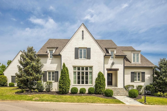 view of front of home with a front lawn, a shingled roof, and brick siding