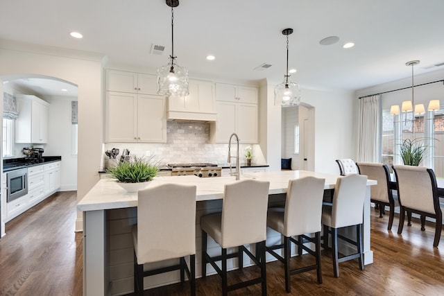 kitchen with stainless steel microwave, tasteful backsplash, visible vents, and arched walkways