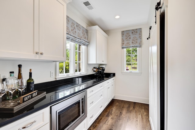 kitchen with stainless steel microwave, dark wood-type flooring, visible vents, white cabinetry, and baseboards