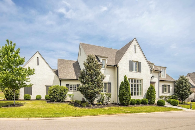 view of front of property with brick siding, a front lawn, and roof with shingles