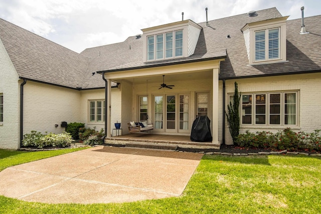 rear view of house with a patio area, a shingled roof, a lawn, a ceiling fan, and brick siding