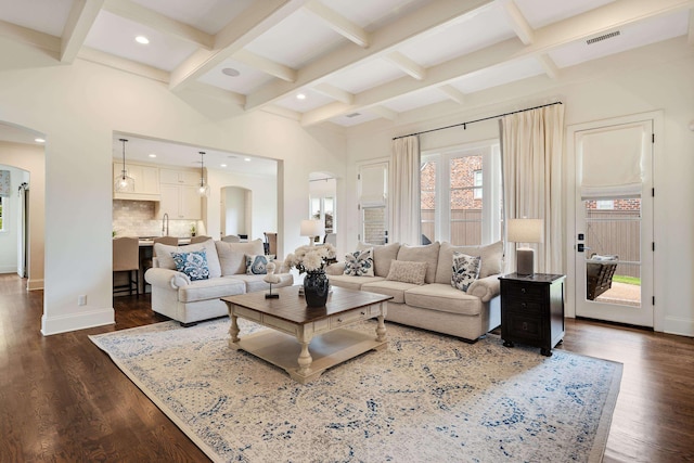 living room with arched walkways, coffered ceiling, beamed ceiling, baseboards, and dark wood-type flooring