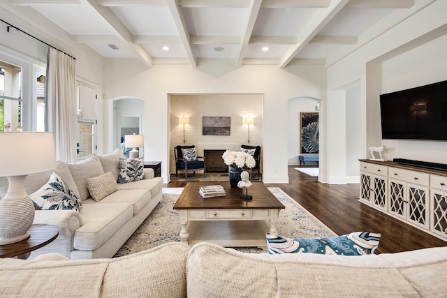 living area featuring arched walkways, coffered ceiling, wood finished floors, and beamed ceiling