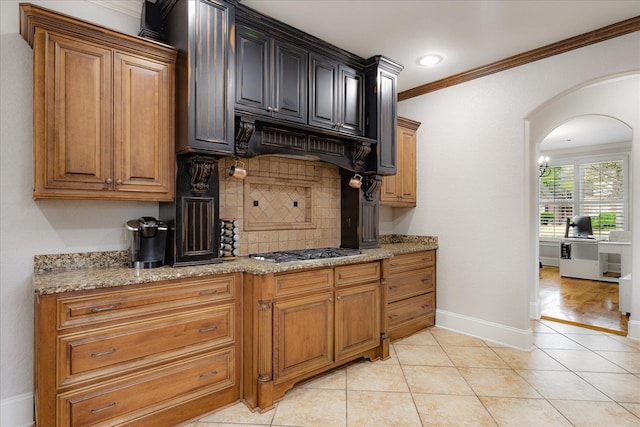 kitchen featuring stainless steel gas cooktop, arched walkways, light stone counters, ornamental molding, and backsplash